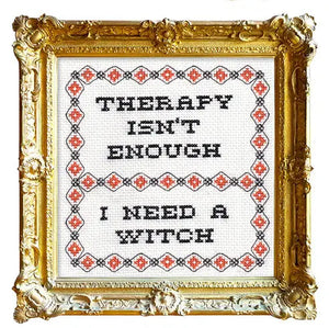 Gold framed cross stitch piece with text that reads "THERAPY ISN'T ENOUGH/I NEED A WITCH" with a patterned border. 
