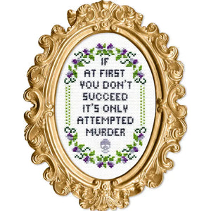 Decorative gold frame with cross-stitched text that says "If at first you don't succeed it's only attempted murder" and floral patterns on a white background