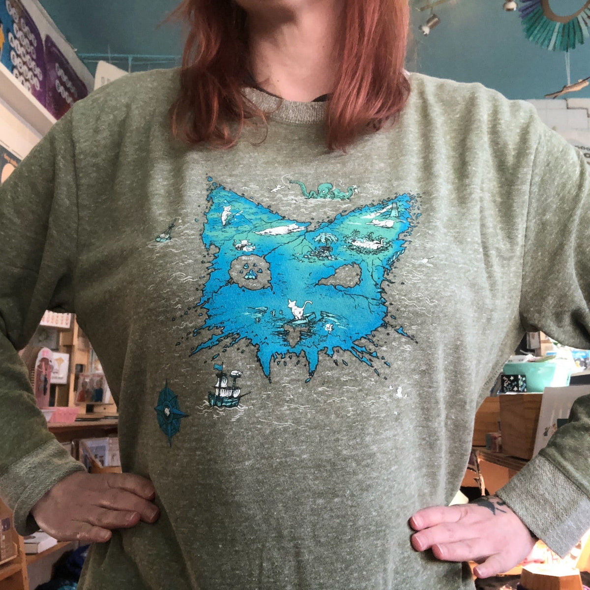 Person wearing a green sweater with a blue cat design in a store setting. 