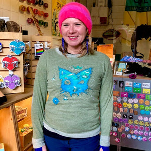 Person wearing a green sweater with a blue treasure map in the shape of a cat-head in a store setting. 