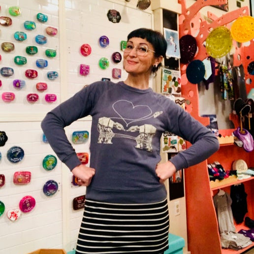 Person wearing a sweater with Love AT-AT First Sight design in a colorful store setting. 