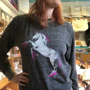 Person wearing a gray sweater with a roller skating unicorn graphic in a store setting. 