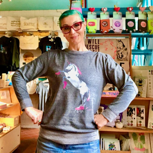 Person wearing a gray sweater with a screenprinted design of a roller skating unicorn in a store setting. 