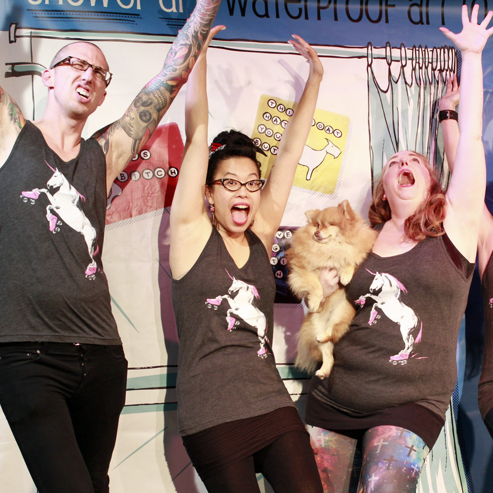 A group of people - all wearing roller skating unicorn tank tops - throwing their hands in the air with excitement. 