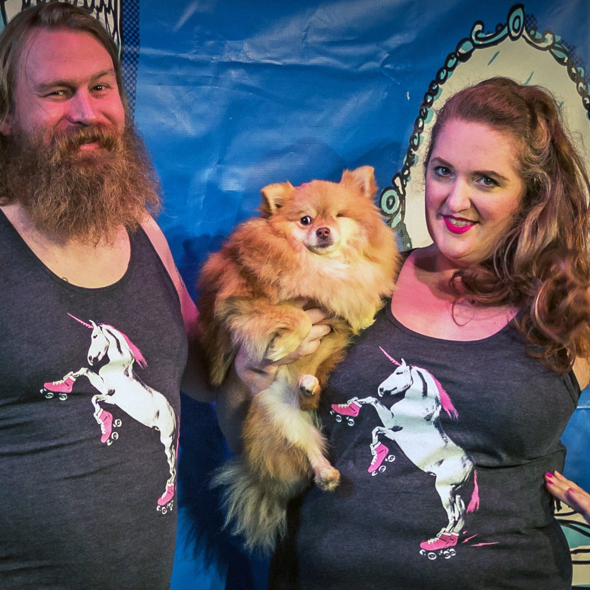 Two people wearing roller skating unicorn tank tops and holding a small dog with one eye. 