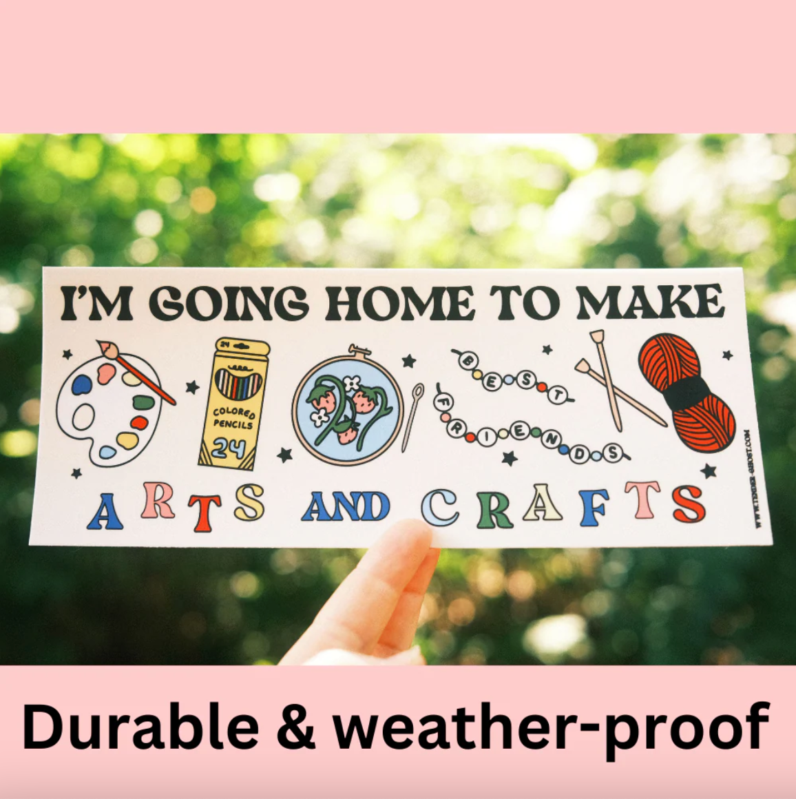 Fingers holding a bumper sticker that says "I'm going home to make arts and crafts" and has cartoon drawings of a paint palette, colored pencils, embroidery, beaded bracelets, knitting needles, and yarn. 