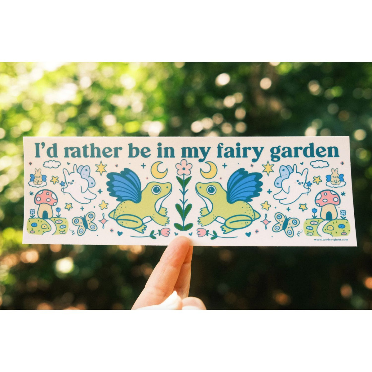 Sticker with fairy garden design held in front of a blurred green background
