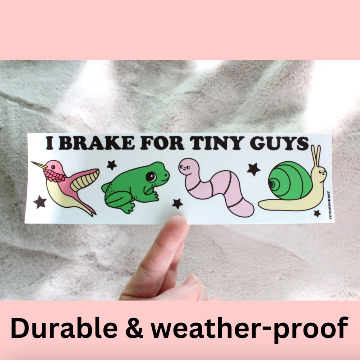 Sticker with cartoon animals and text 'I Brake for Tiny Guys' held by a hand on a textured surface.