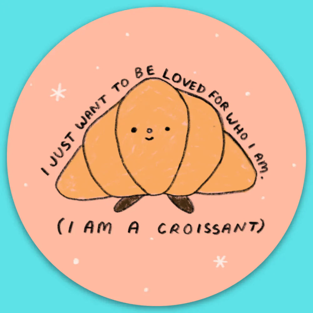 A round sticker with a cartoon drawing of a croissant that says "I just want to be loved for who I am. (I am a croissant)"