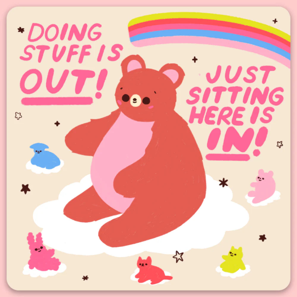 A sticker with text that says "doing stuff is out! just sitting here is in!" and has a bear sitting on a cloud and a rainbow in the background. 