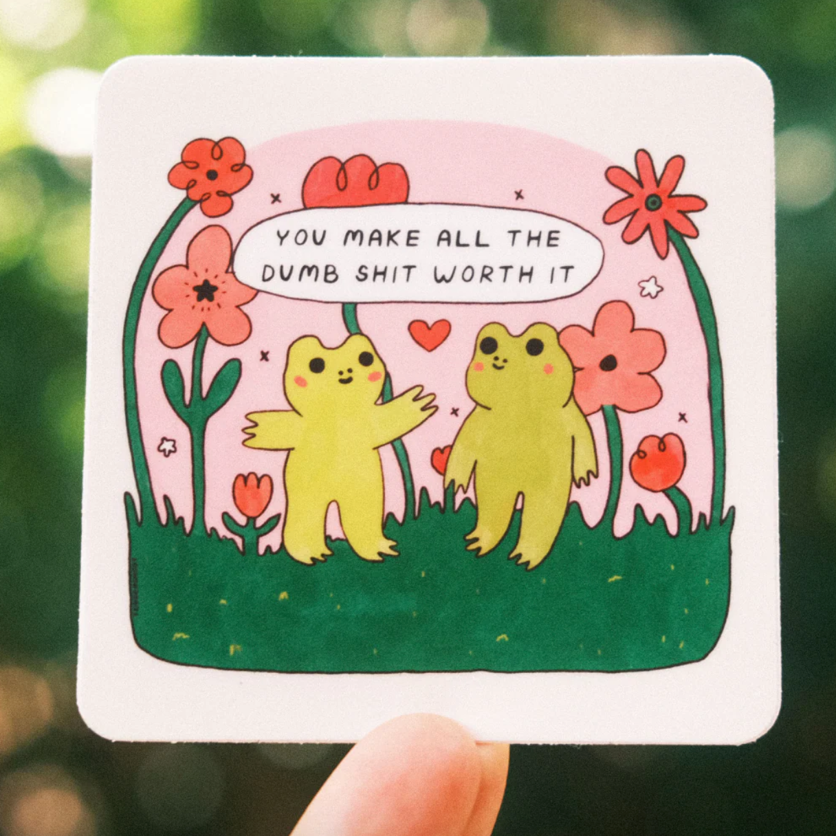 Cartoon illustration of two frogs and flowers with a text that says "you make all the dumb shit worth it" on a white background.