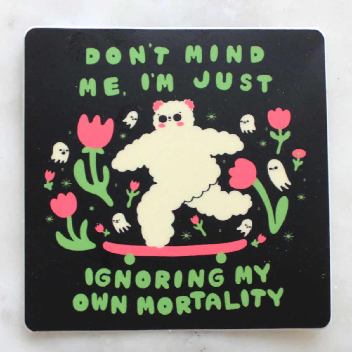 Sticker with a cartoon character on a skateboard, flowers, and text that says "don't mind me, I'm just ignoring my own mortality" on a black background.