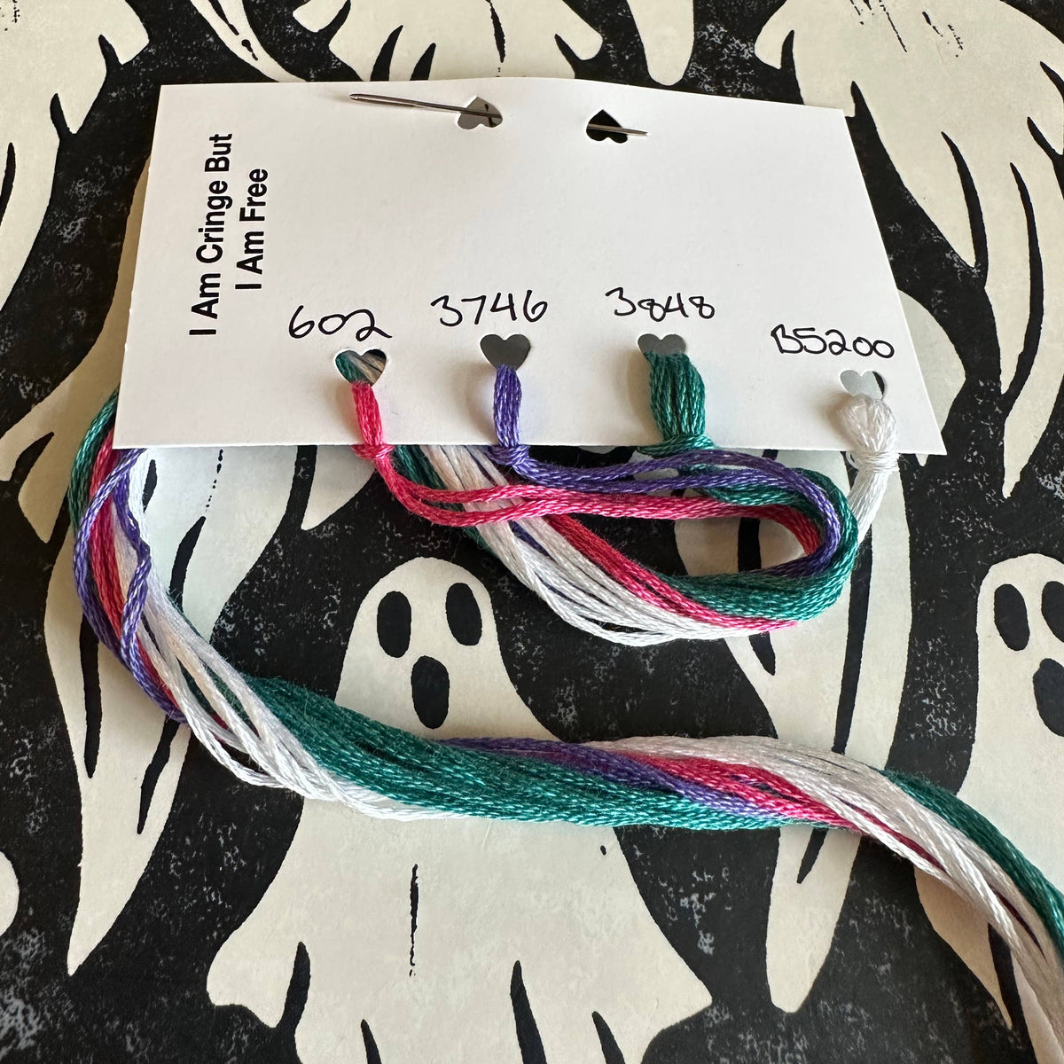 Colorful embroidery floss on a card with ghost patterns in the background