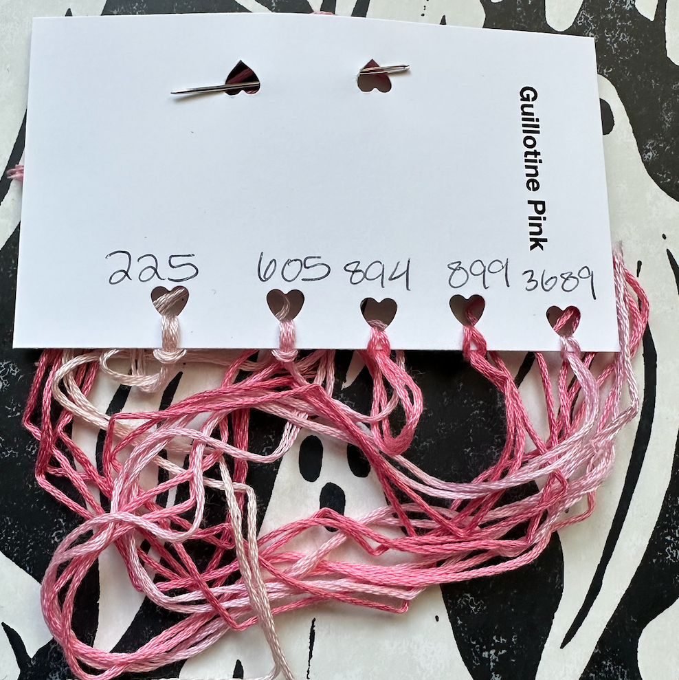 Pink embroidery floss on a branded card against a black and white patterned background.