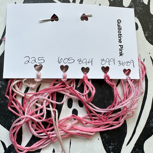 Pink embroidery floss on a branded card against a black and white patterned background.