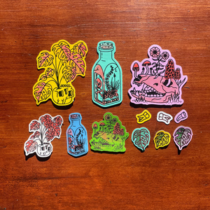 12 bone-themed stickers in various bright colors, including a skull full of monstera leaves, a bottle terrarium, and an animal skull with mushrooms and flowers growing out of it. 