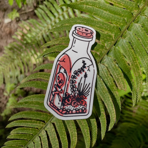 White sticker of a bottle with a skull and bones on it and a terrarium inside with red shading against a background of fern leaves. 