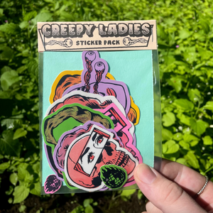Sticker pack of women's faces and skulls and eyeballs with the text "Creepy Ladies sticker pack" held against a background of plants. 