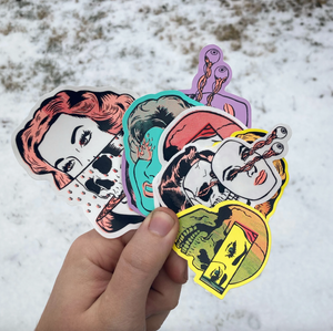 A hand holding a stack of stickers of skulls and women's faces against a white background. 