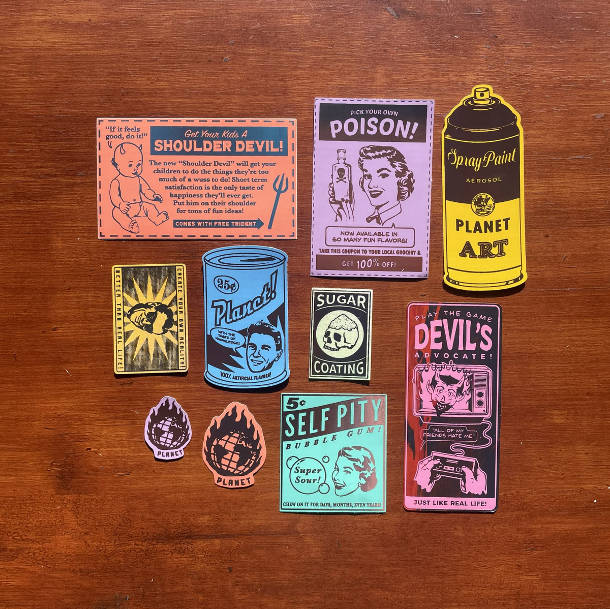 10 stickers of varying colors, shapes, and sizes depicting vintage style tongue-in-cheek ads against a wooden background. 