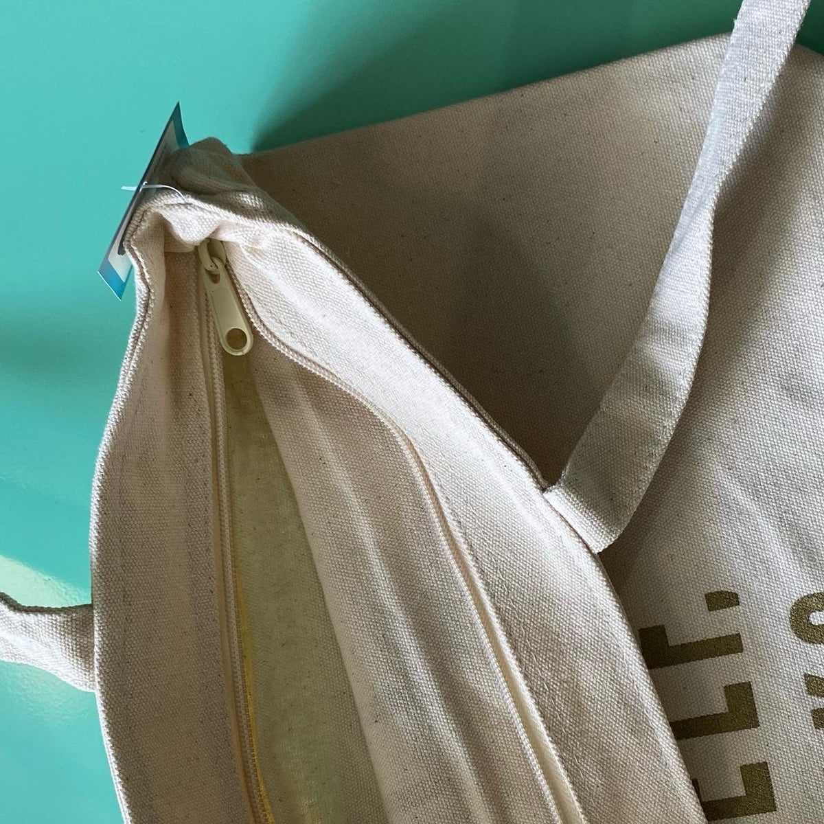 Close up of the zipper closure on a cream colored canvas tote bag.