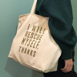 A cream colored canvas tote bag with gold lettering that says, "I will rescue myself, thanks."
