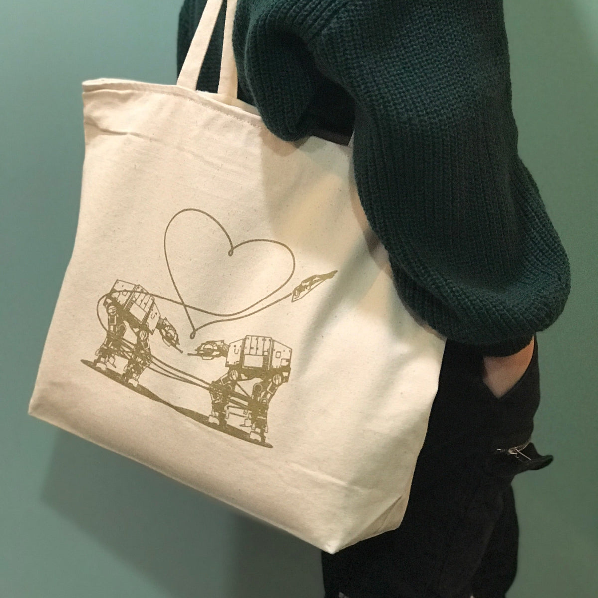 Cream colored tote bag with the Love AT-AT First Sight design printed in gold ink. 