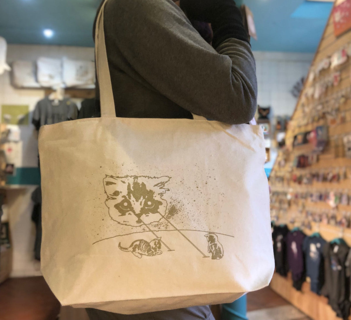 A person modeling a natural color tote bag with a cat design printed in gold ink. 