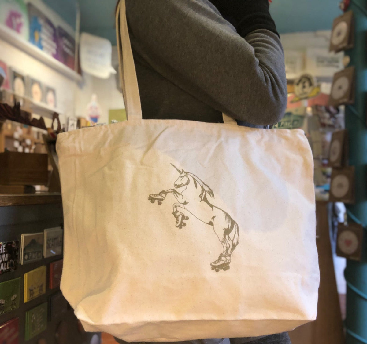 A cream colored tote bag with a roller skating unicorn printed in gold ink. 