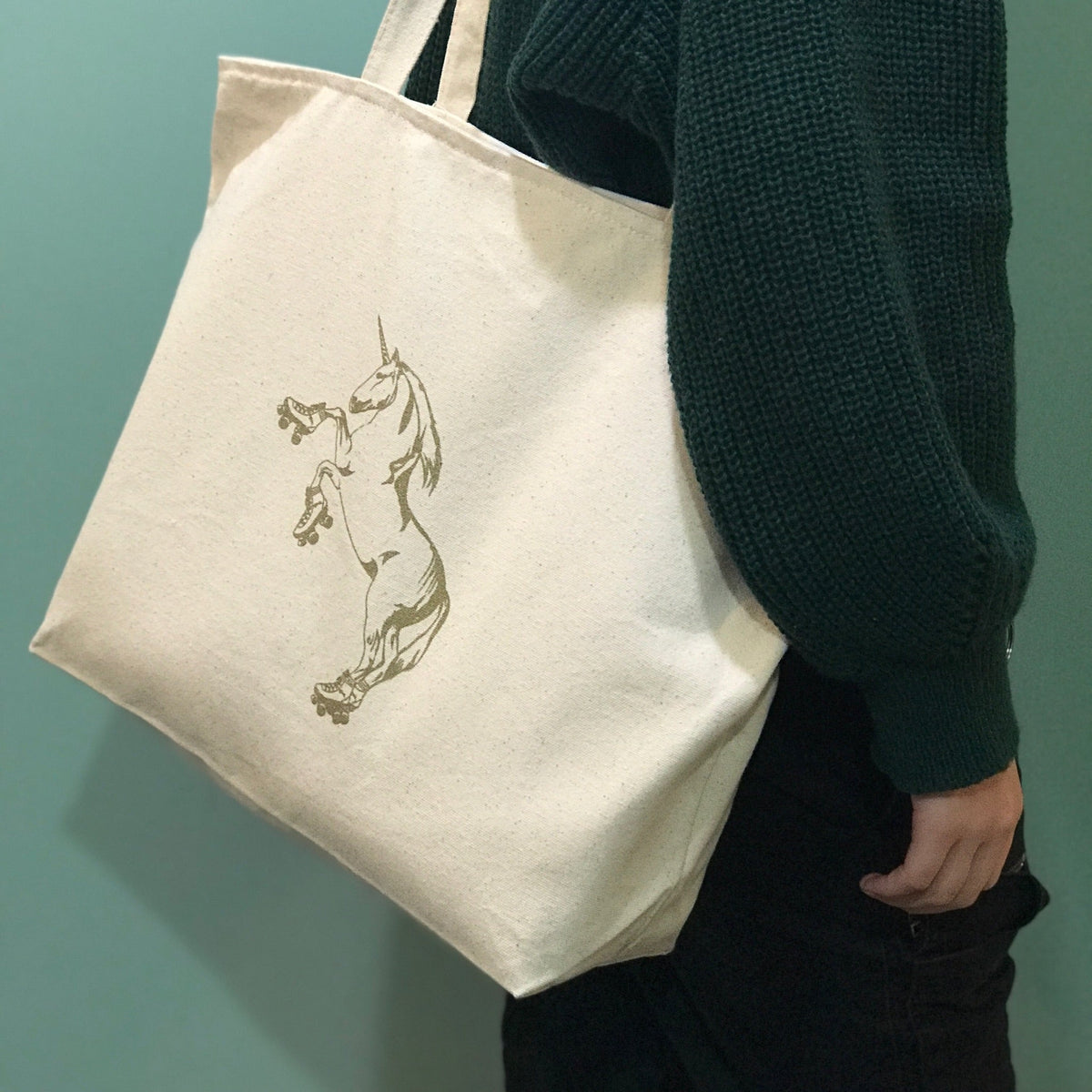A cream colored tote bag with a roller skating unicorn printed in gold ink. 