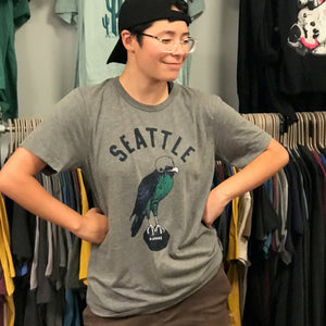 Person wearing a 'Seattle' t-shirt with a bird graphic in a clothing store.