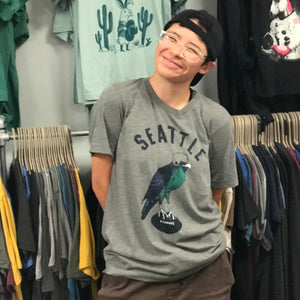 Person wearing a 'Seattle SeaBIRD' t-shirt with a bird graphic in a clothing store.
