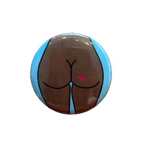 Round button featuring a design of a butt with a heart tattoo against a light blue background. 