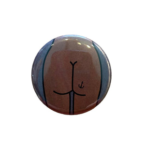 Round button featuring a design of a butt with an anchor tattoo against a dark gray background. 