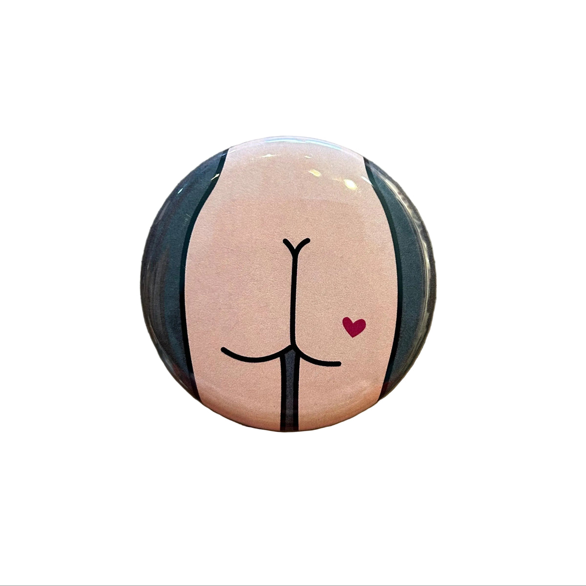 Round button with a drawing of a butt with a heart on a wooden surface