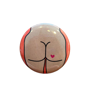 Round button with a design of a butt with a heart tattoo against an orange background. 