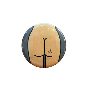 Round pin featuring a drawing of a butt with an anchor tattoo on a dark gray background. 