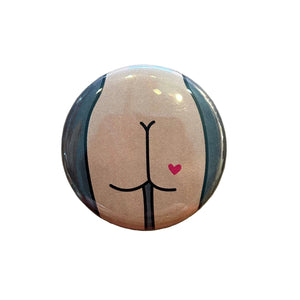 Round button with a drawing of a tan butt with a heart tattoo against a dark gray background. 