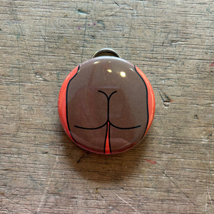Bottle opener keychain featuring a design of a brown butt with an orange background on top of a wooden surface. 