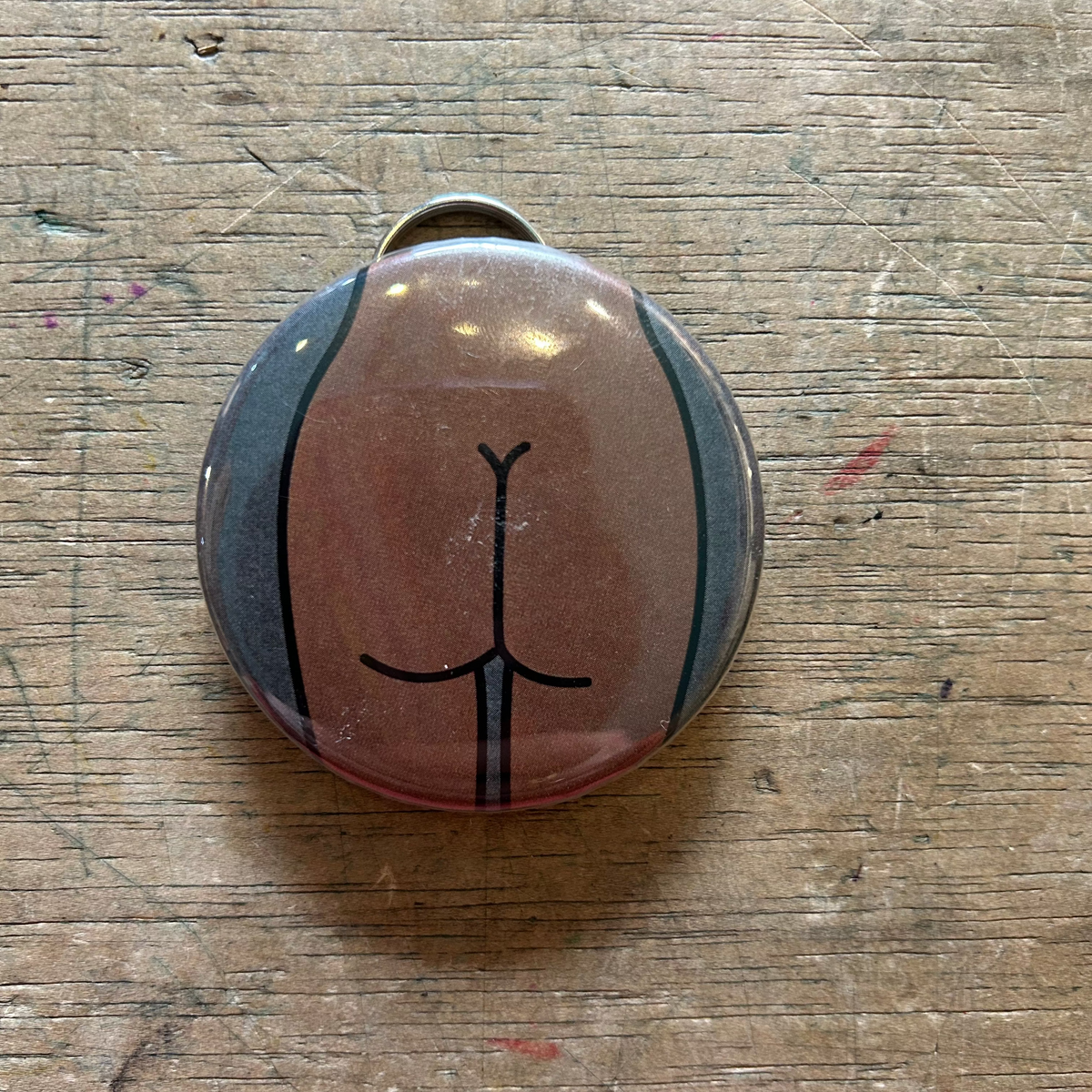 Bottle opener keychain featuring a design of a brown butt with a gray background on top of a wooden surface. 