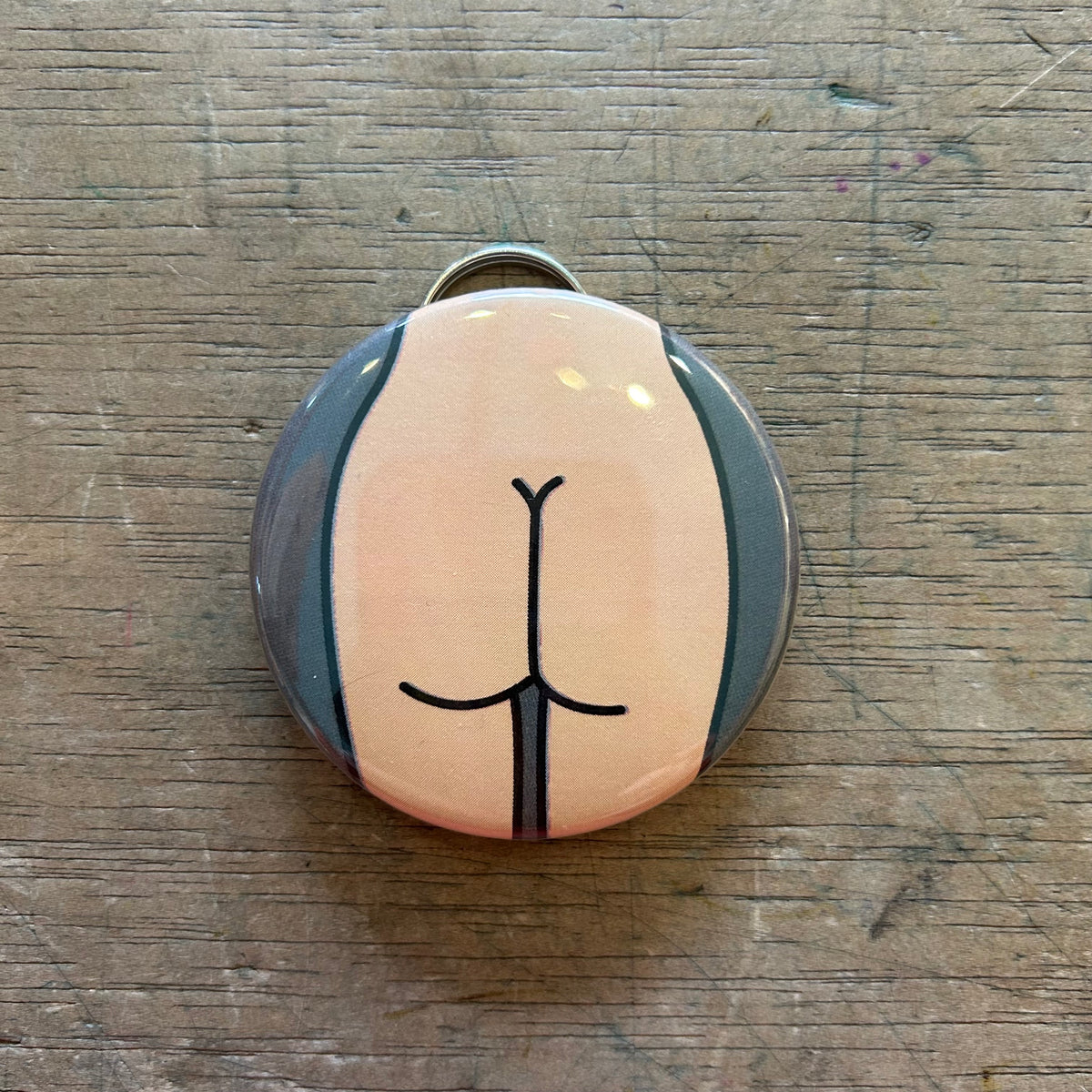 A bottle opener keychain featuring a light colored butt with a gray background on top of a wooden surface. 