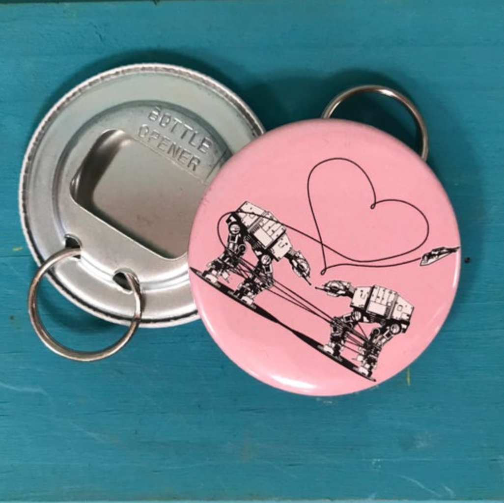 Round pink bottle opener keychain featuring the Love AT-AT First Sight design against a bright blue background. 