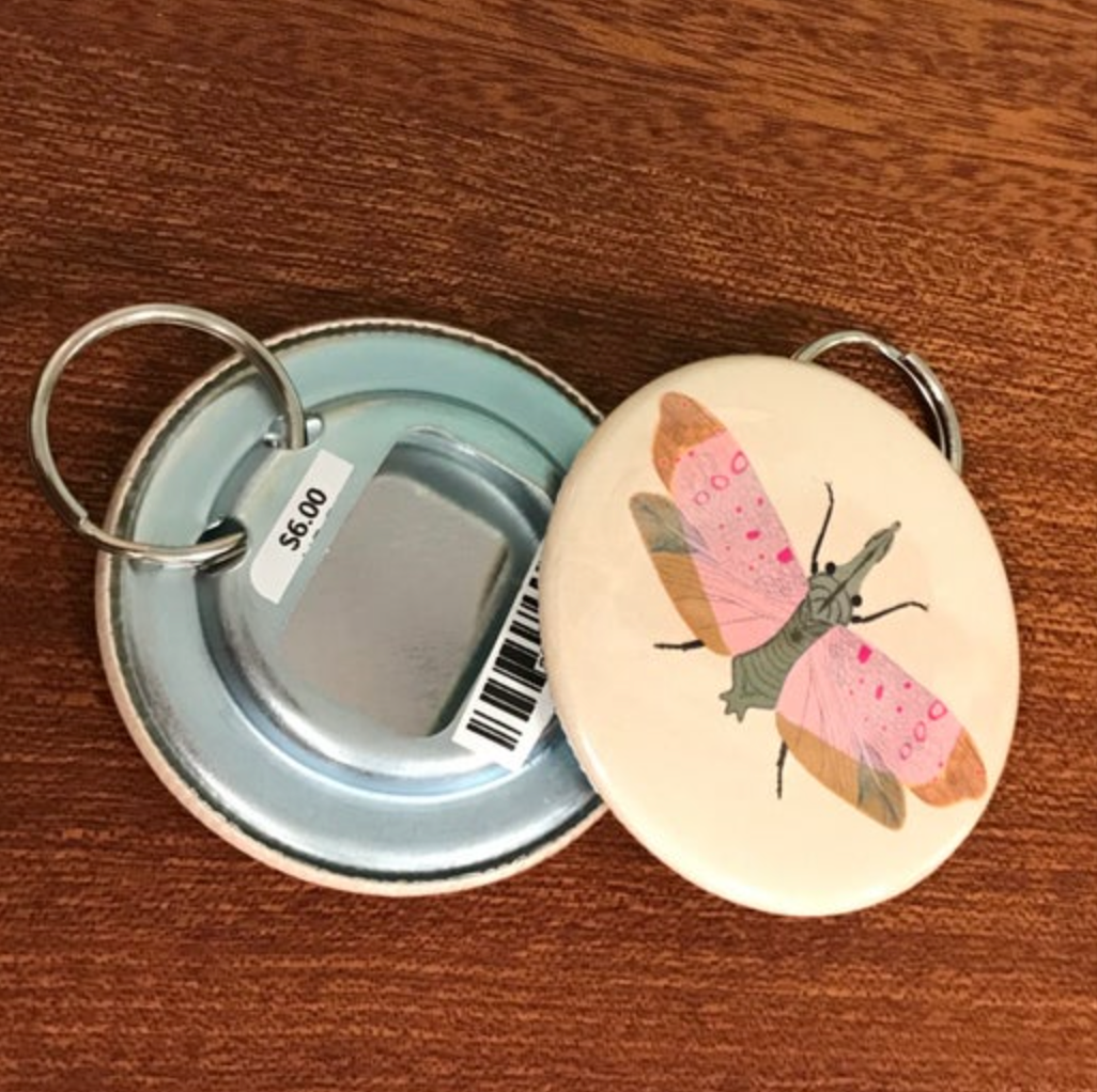 Round keychain with moth design on a wooden surface