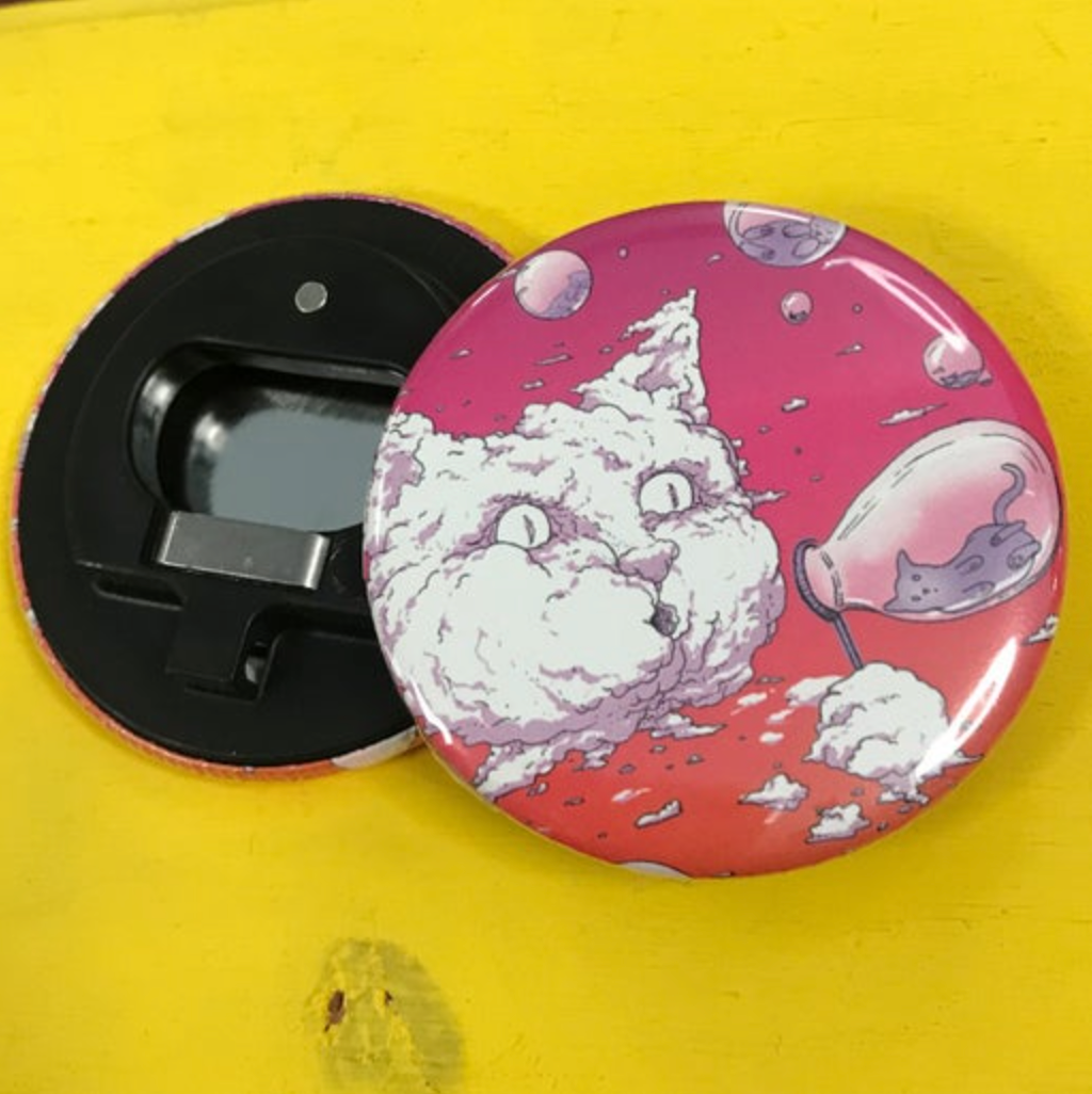 Bottle opener magnet featuring a cat blowing bubbles against a pink background on top of a bright yellow surface. 