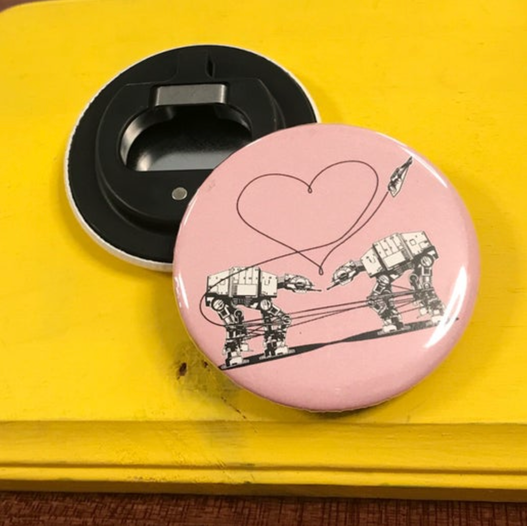 Round pink bottle opener magnet featuring the Love AT-AT First Sight design on top of a yellow surface.