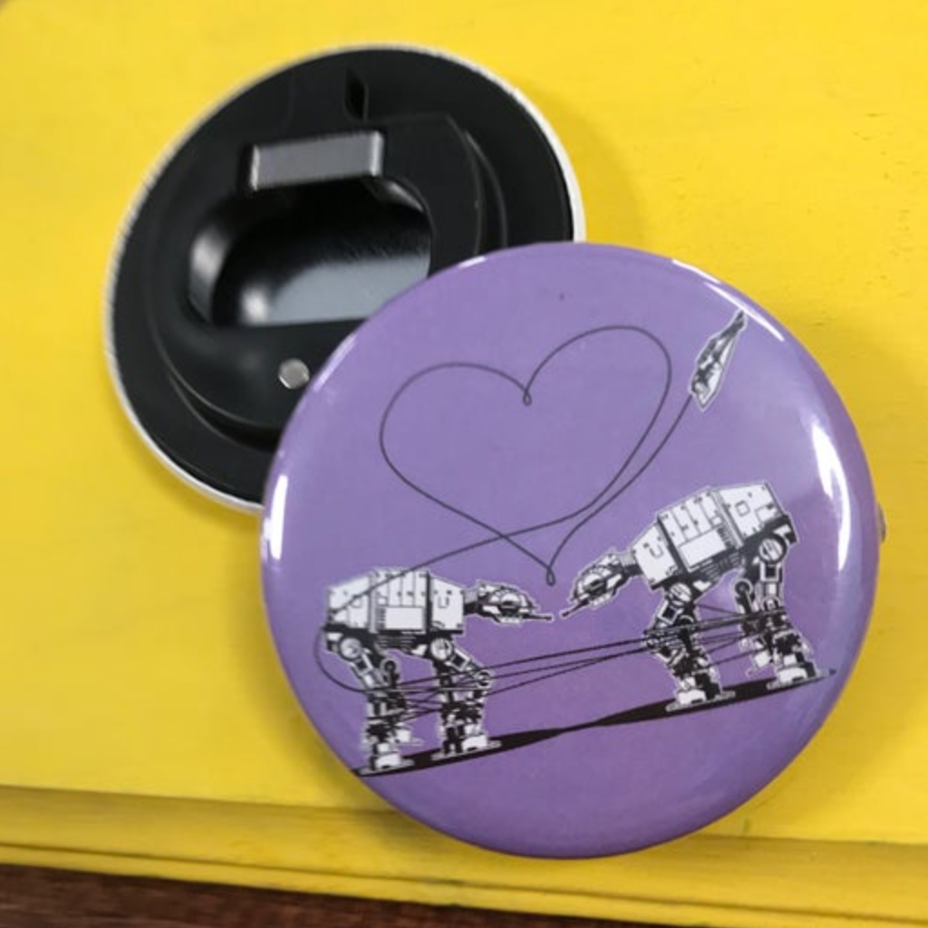 Round purple bottle opener magnet featuring the Love AT-AT First Sight design on top of a yellow surface. 