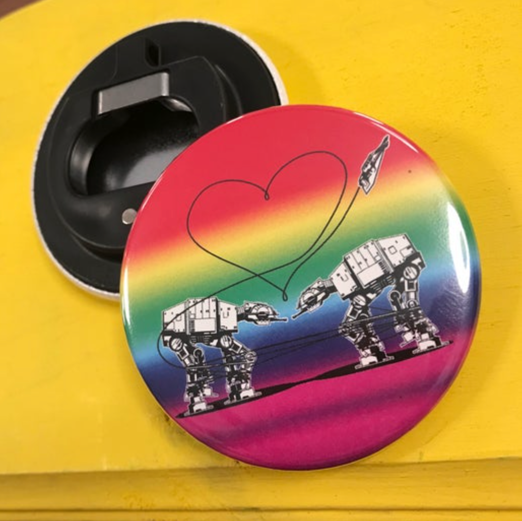 Round rainbow bottle opener magnet featuring the Love AT-AT First Sight design on top of a yellow surface. 