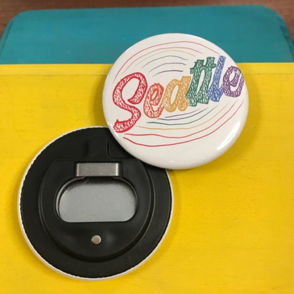 Round bottle opener magnet featuring the word "Seattle" in rainbow letters. 