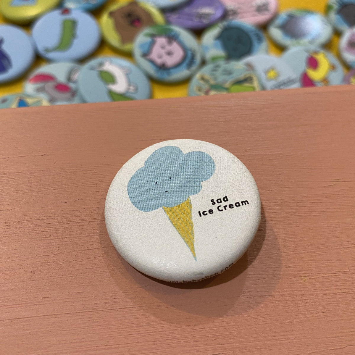 Button badge with an ice cream cone design labeled 'Sad Ice Cream' on a wooden surface.