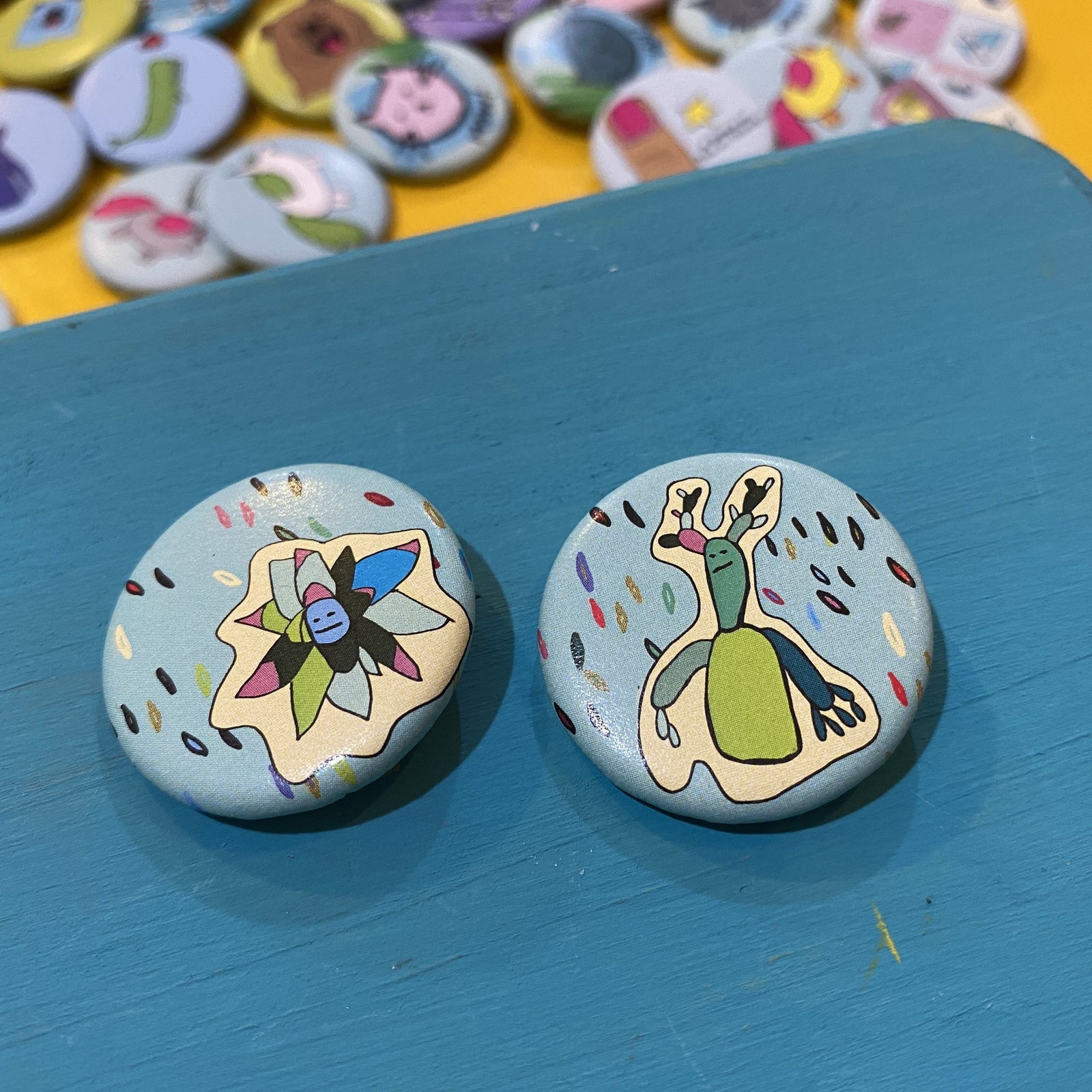 Two colorful buttons with cartoon designs on a blue surface, with more buttons in the background.
